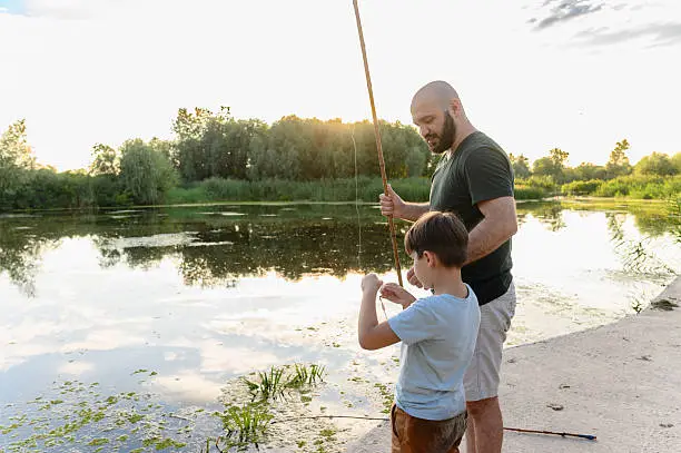 A father and son fishing together at a pond at sunset