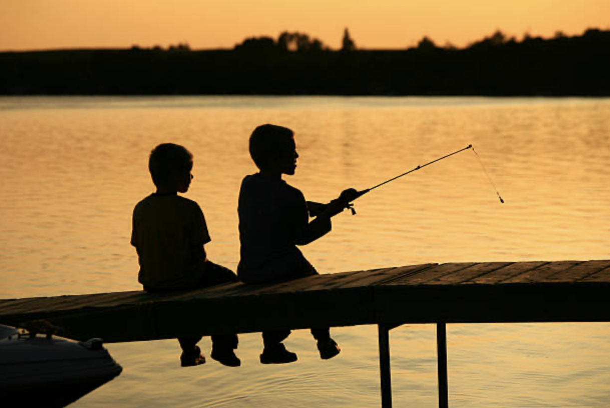 Two children fishing from a dock at sunset